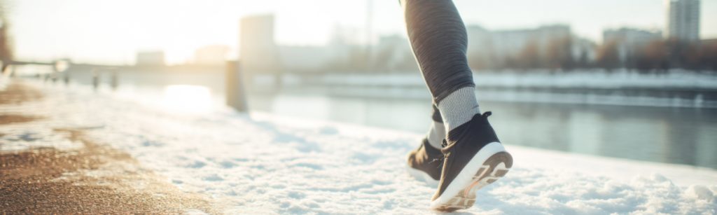 Runners legs in modern sneakers on a snow-covered path by a river during winter afternoon