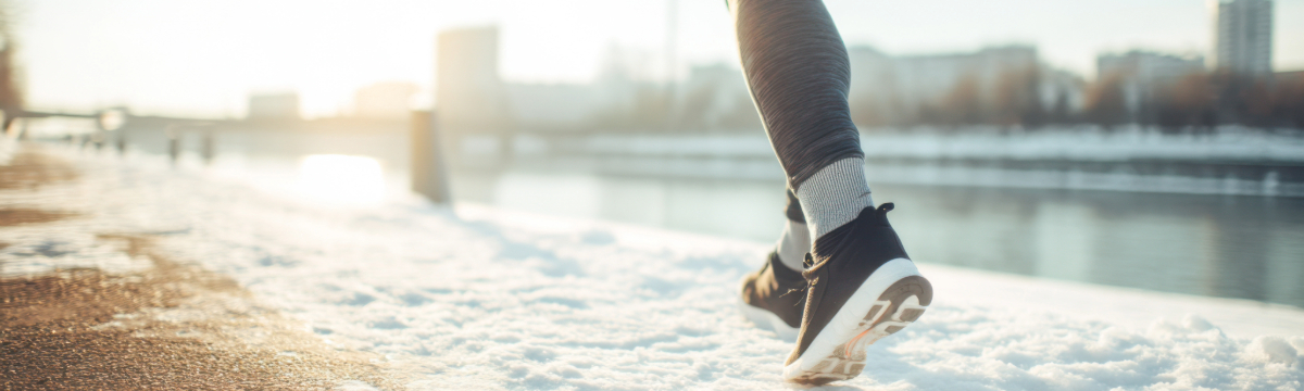 Runners legs in modern sneakers on a snow-covered path by a river during winter afternoon