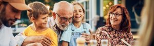 Older adults and children sitting together at an outdoor table with food and drinks.