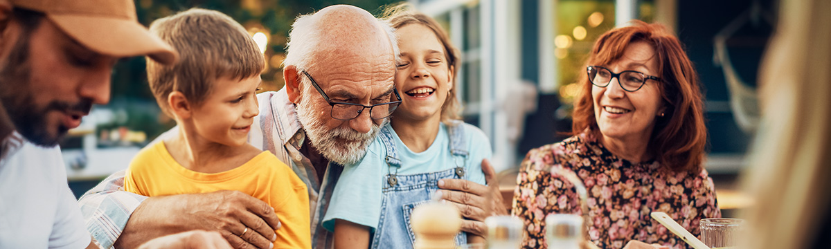 Older adults and children sitting together at an outdoor table with food and drinks.