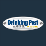 Logo of Drinking Post Waterer with a metallic oval background, "Drinking Post Waterer" in blue, and "Of Laramie" in yellow below.