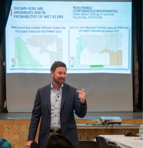 A presenter discusses precipitation patterns and climate outlook maps projected behind him