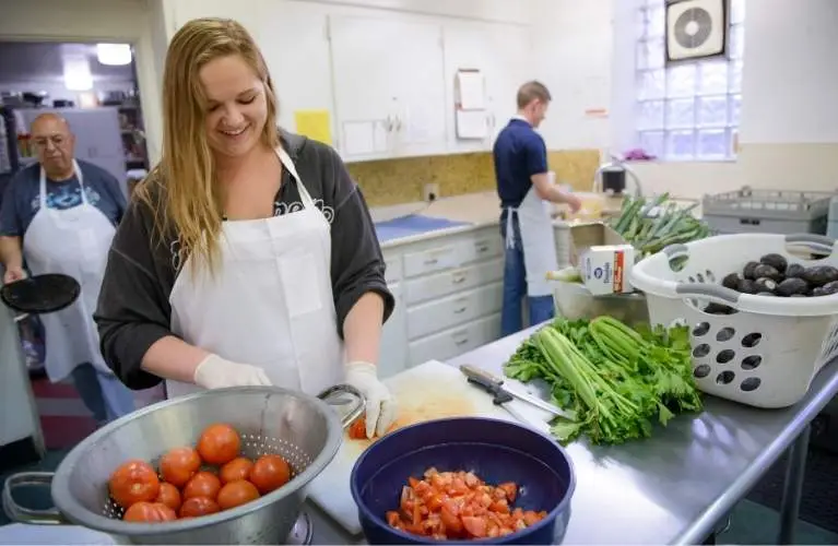 woman smiling in kitchen cutting up tomatoes