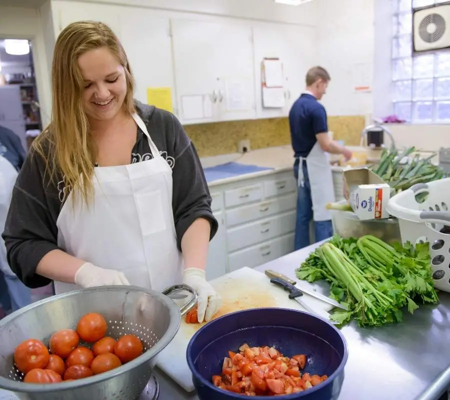 woman smiling in kitchen cutting up tomatoes