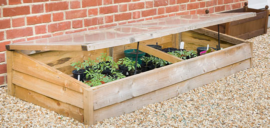 Wood frame growing bed with clear cover next to brick house 