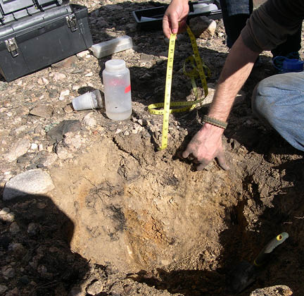 Students examining the sides of a 16 to 24-inch deep hole they dug in the rocky ground 