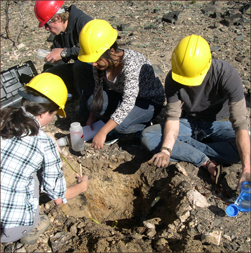4 university students in jeans and hard hats taking soil samples from burned  rock ground 