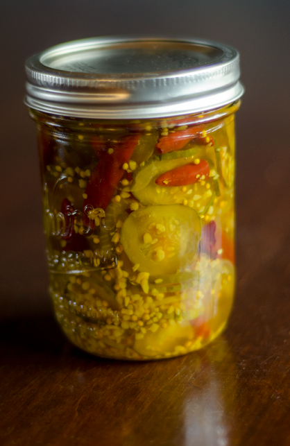 Small mason jar with sliced pickes and red chili peppers in a spice-laden brine 