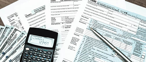 Calculator,  100 bills and pen on top of 1040 tax forms