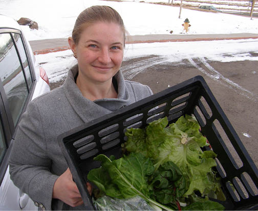 Woman holding black plastic crate with fresh leafy green vegetables