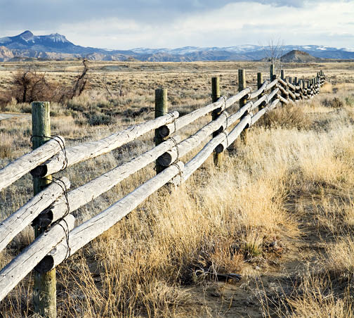 photo of wood rail fence running through rangeland with mountains in the background