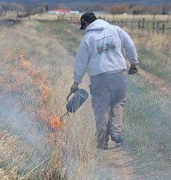 Man walking along dirt road and burning ditch to one side 