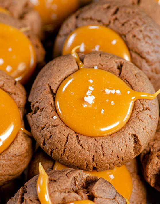 A close up of chocolate thumbprint cookies with a golden glaze in the center. 