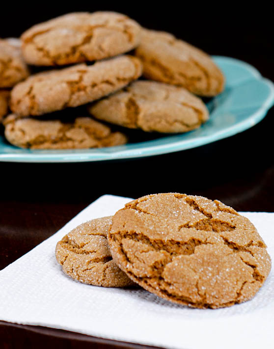 Two crisp gingersnaps placed on a white napkin and a blue plate of crisp gingersnaps in the background. 