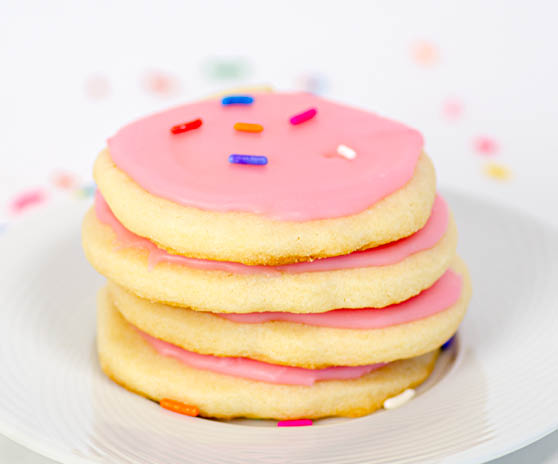 A stack of four sugar cookies with pink frosting and sprinkles. 