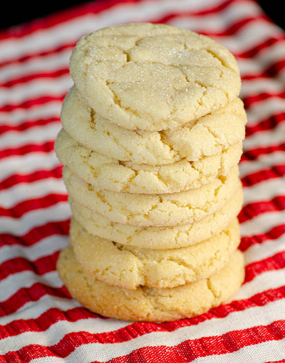 A stack of seven drop sugar cookies, on top of a red and white striped dish towel. 