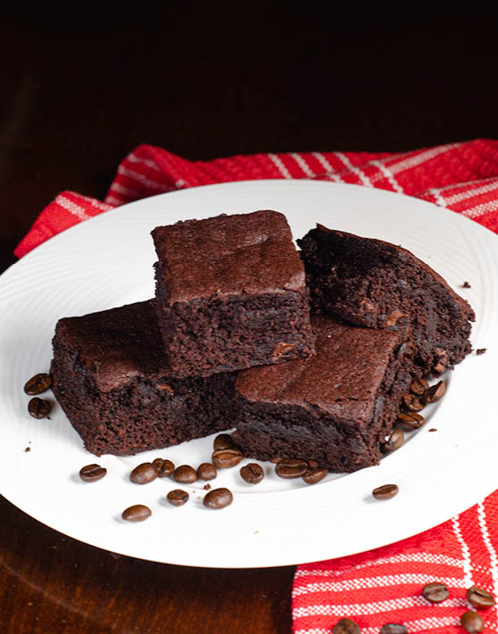 A plate of brownies set on top of a red and white dish towel. 
