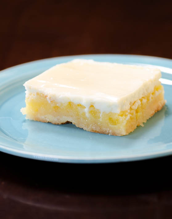 A rectangle piece of sour cream topped lemon bars placed on a blue plate. 