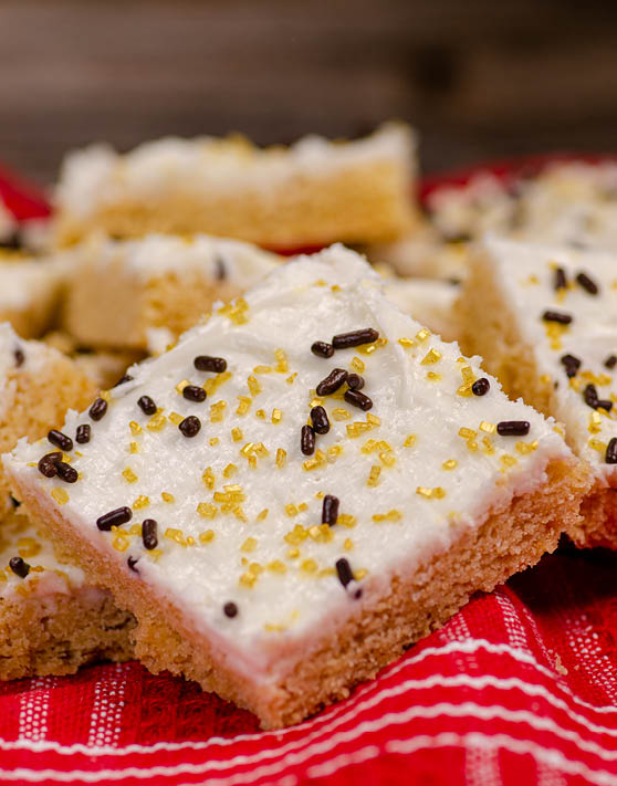 Scrumptious sugar cookie bars on top of a white and red striped dish cloth. 