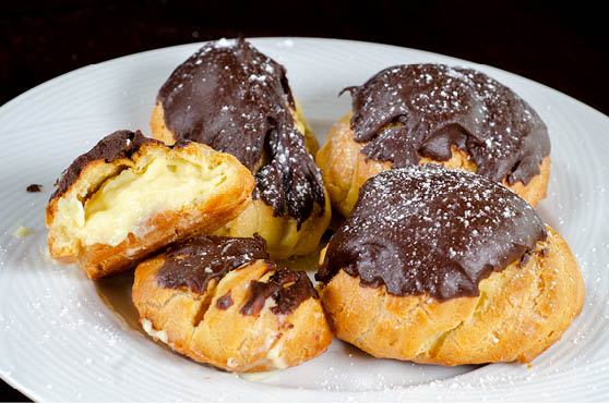 A white plate with five cream puffs covered with a chocolate frosting. 
