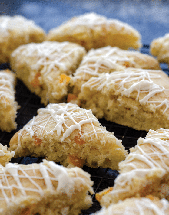 Scones with white drizzled frosting placed on a cooling rack. 