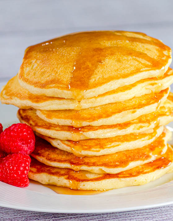 A stack of pankcakes with raspberries to the left, placed on a white plate. 