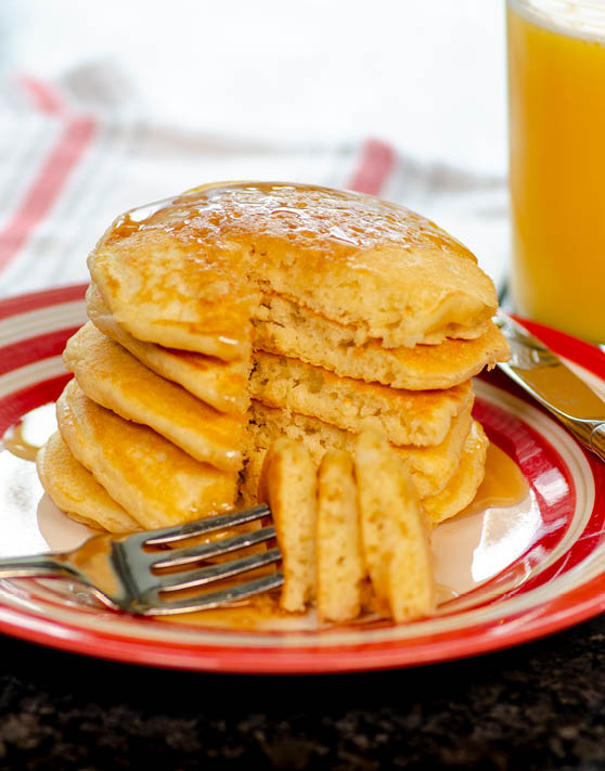 A stack of fabulous fluffy pancakes, with a triangular piece cut out of the stack, and a fork with the piece of pancake placed in front of the stack. 