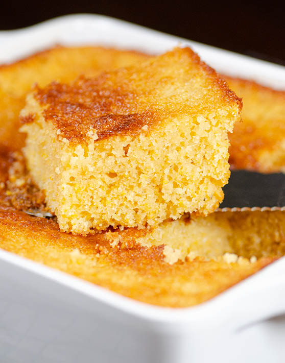 A piece of honey buttermilk cornbread freshly cut out of a pan of cornbread. 
