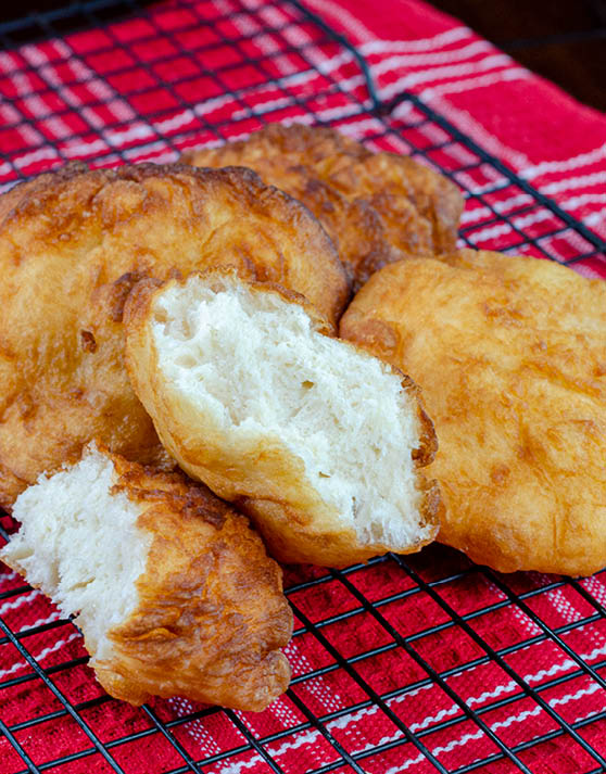 Native american fry bread placed on a cooling rack with a red and white dish towel under it. 