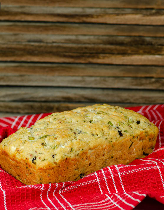 Bacon, cheese, and olive batter loaf of bread placed on a red and white dish towel. 