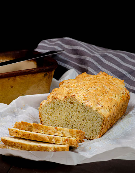 A loaf of buttermilk cheese batter bread, half of which is sliced into pieces, while the rest of the loaf remains uncut. 