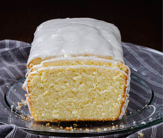 A loaf of iced lemon bread with two sliced pieces. 