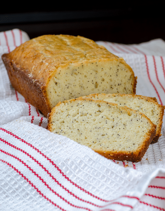 A loaf of orange glazed poppy seed bread placed on top of a white and red towel. 