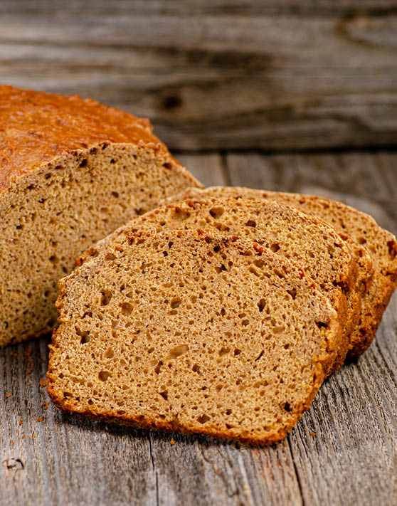 A loaf of brown soda bread with three slices cut from the loaf. 