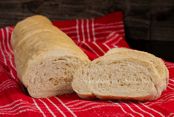 A french bread loaf with two slices placed on top of a red and white striped dish towel. 