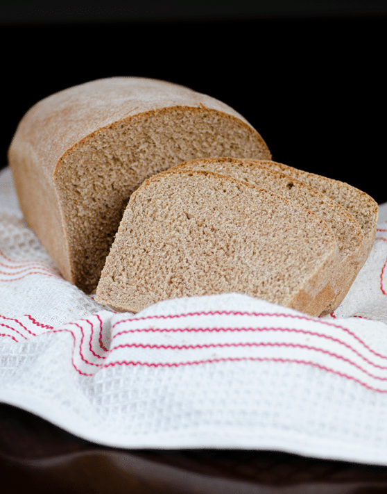Honey whole wheat bread with two slices cut out of it placed on a white and red dish towel. 
