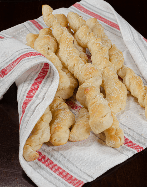 Twisted parmesan garlic breadsticks placed on top of a red, white, and grey dish towel. 