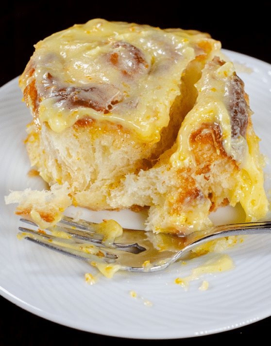 An orange sweet roll placed on a white plate and fork in the foreground. 
