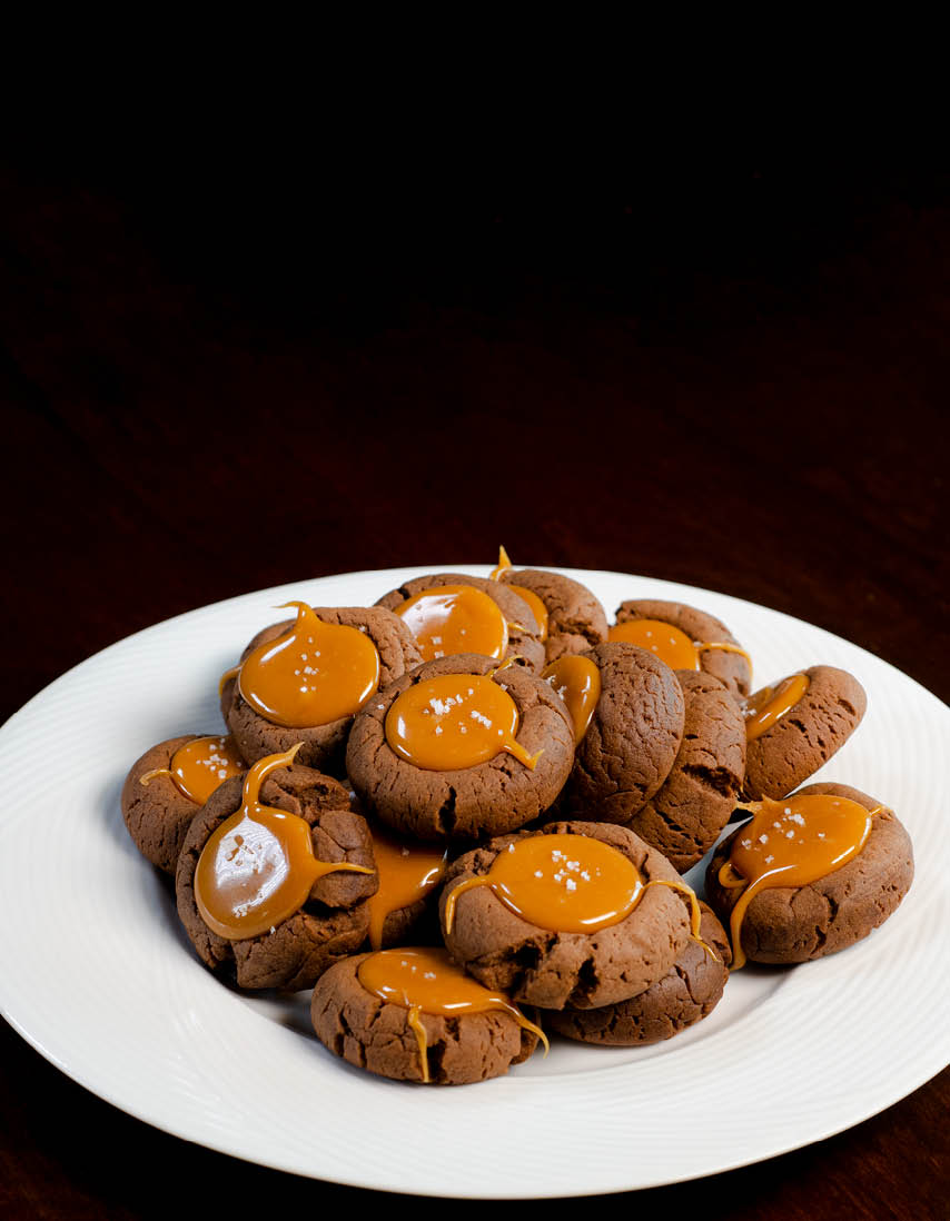 A white plate of brown cookies with a carmel looking substance in the center. 