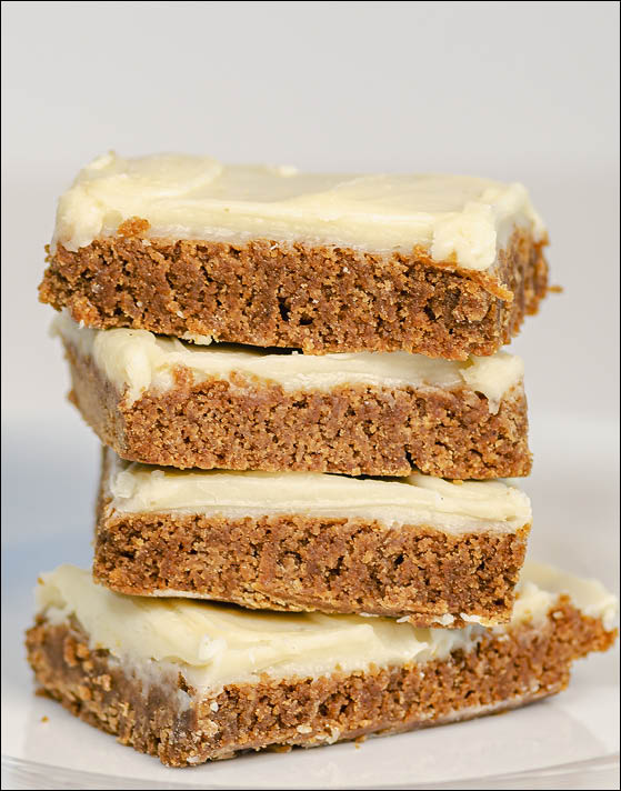 Four cream cheese frosted gingerbread bars stacked on top of eachother placed on a white paper towel. 