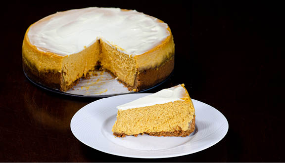 A piece of pumpkin cheesecake with gingersnap crust on a white plate with the cheesecake in the background. 
