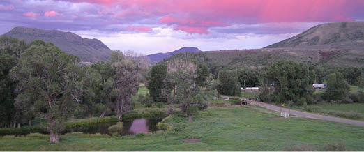 A scenic view of Battle Creek, Little Snake River Valley, with pink and purple sunset with hills and trees  