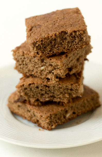 4 light brown brownies stacked on a white plate 