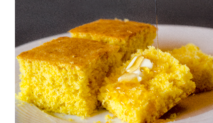 Corn bread on a white plate with a pat of butter and a drizzle of honey from above