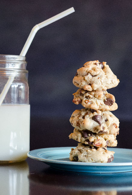 Stack of 5 chocolate chip cookies with pecans on a vintage blue Fiestaware plate  A mason jar of milk and a white straw are on the table next to the plate 
