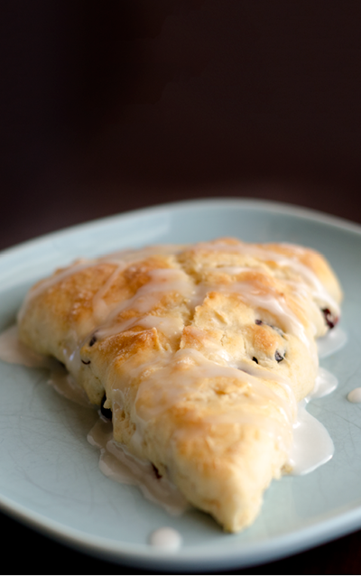Triangle-shaped scone on a blue plate and  drizzled with the powdered sugar glaze 