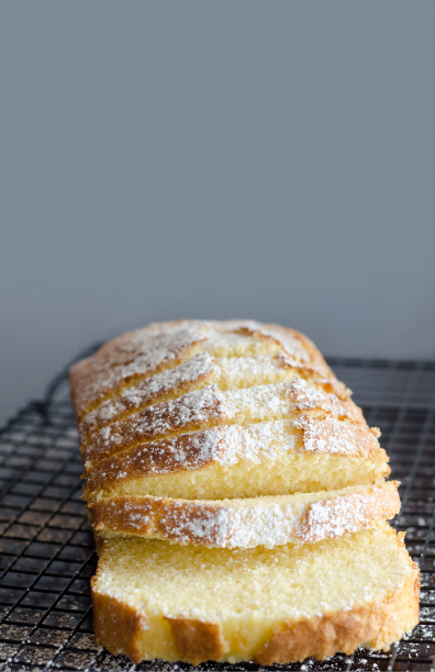 Yellow quick bread dusted with powdered sugar  sliced  and sitting on a black mesh cooling rack 