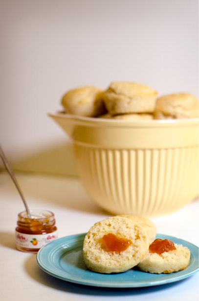 Retro yellow bowl of plain muffins sits in the backround with a blue plate with two muffins  one with strawberry jam  in the foreground 