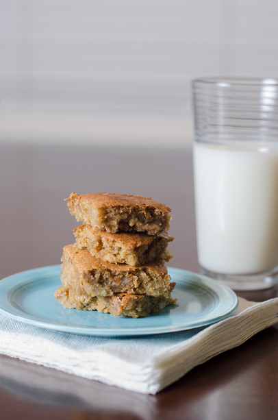 4 bar cookies stacked on a vintage aqua blue Fiestaware plate  The plate is sitting on a stack of napkins  A glass of milk is in the background 