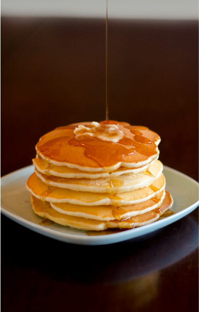 Stack of 6 pancakes  with melted butter pat and maple syrup being poured from above 